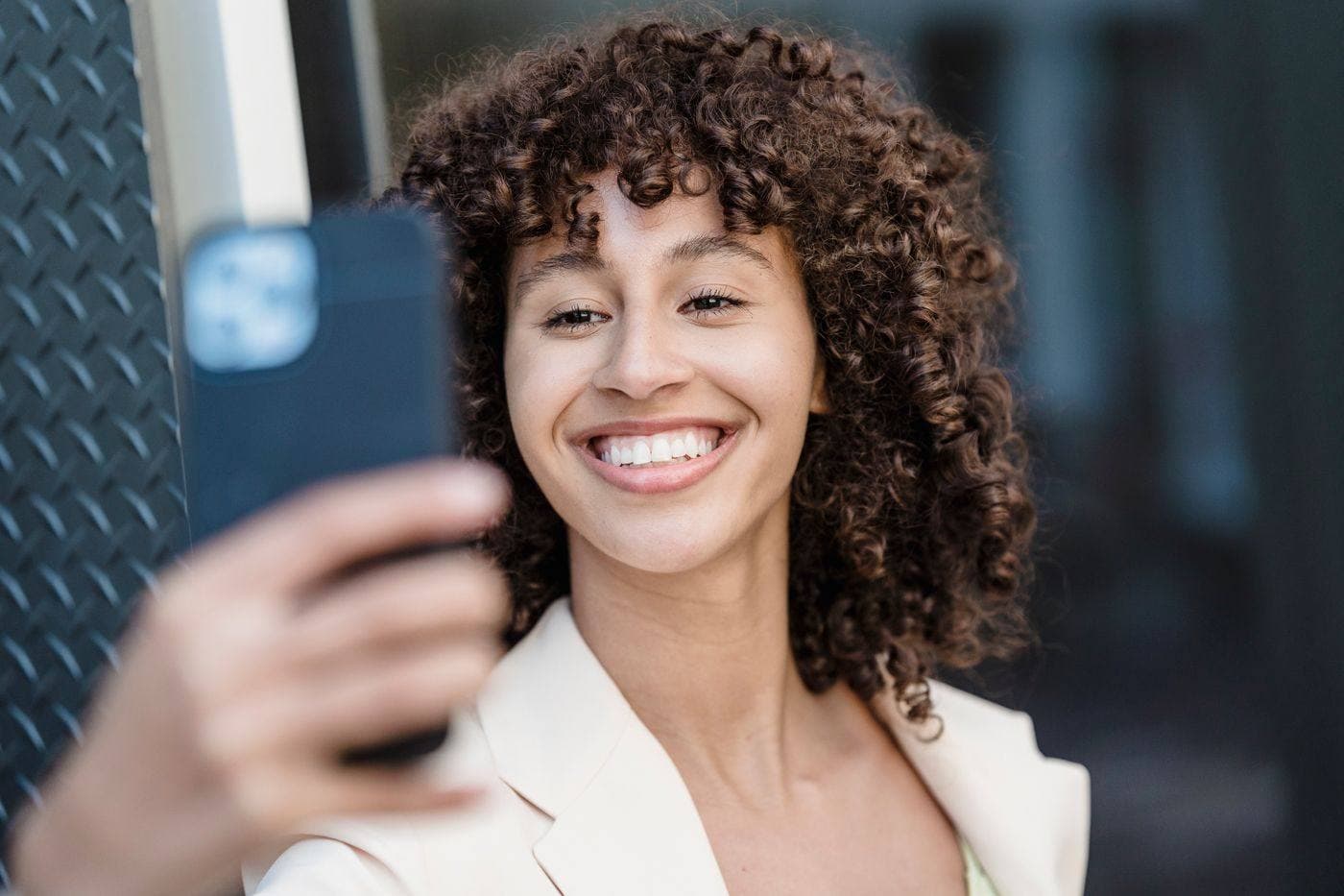 A woman holding up her phone and grinning at what is on the screen.
